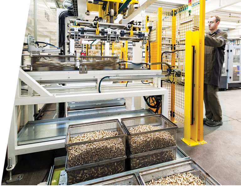 Operatore che lavora su una linea automatizzata di produzione, posizionando componenti all'interno di una macchina industriale, mentre ceste piene di pezzi torniti appena lavati sono pronte per il processo successivo.